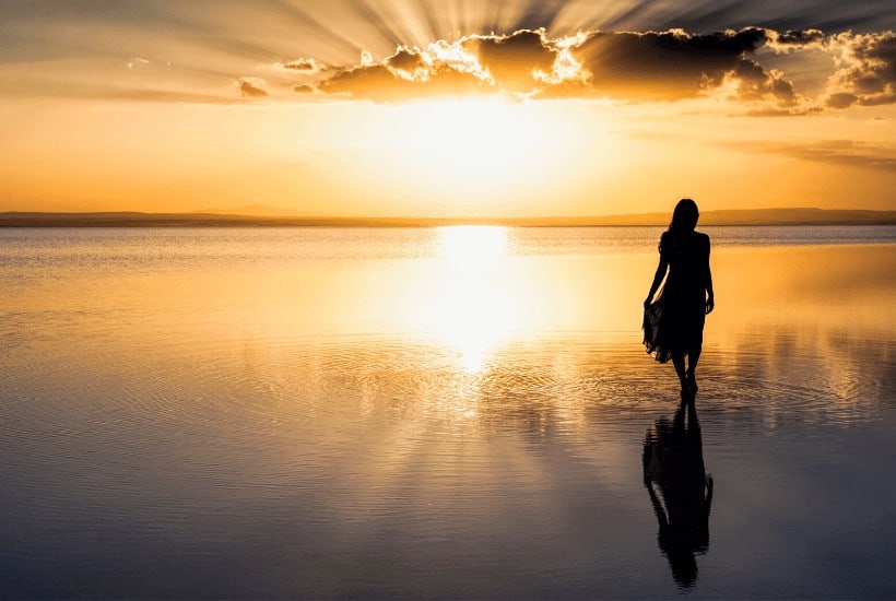 an image of a woman walking the beach with a golden sunset in the background featured image for Do You Know The Importance Of Walking With God?