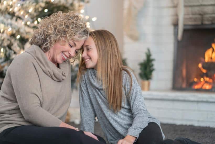 a mother and daughter sitting in the floor by a fireplace touching foreheads with a Christmas tree in the background featured image for How to Find Hope for the Holidays after the Loss of a Parent?