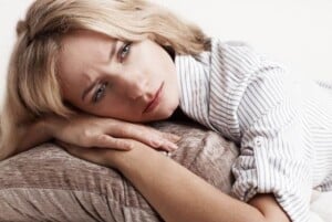 a woman with blonde hair wearing a white shirt lying on a tan sofa hands clasped on the end pillow featured image for 18 Short Prayers About Grief for a Grieving Heart