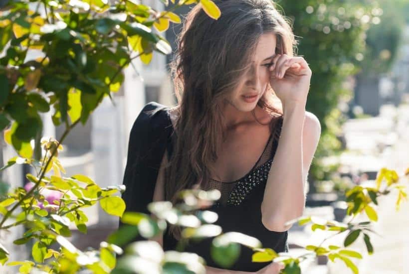 a woman wearing a black dress wiping tears from her eyes surrounded by flowers featured image for 84 Helpful Bible Verses About Grief to Bring You Comfort
